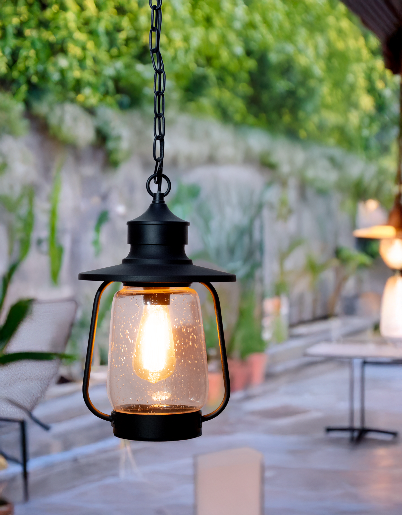 Lantern Hanging Light by Kyess Lighting, suspended in a serene garden setting, casting a warm and inviting glow with its vintage glass enclosure